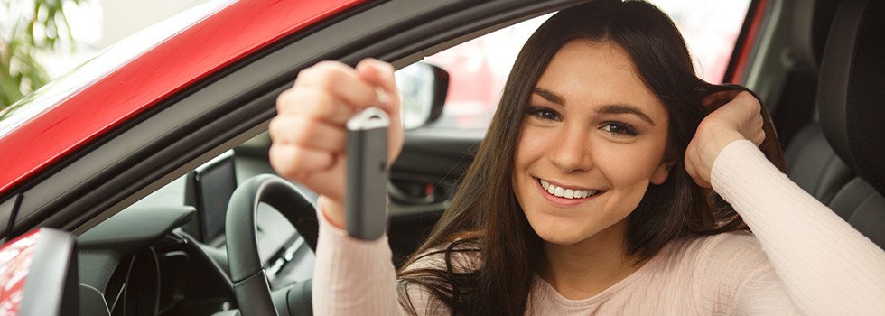 young girl sitting in red car holding key