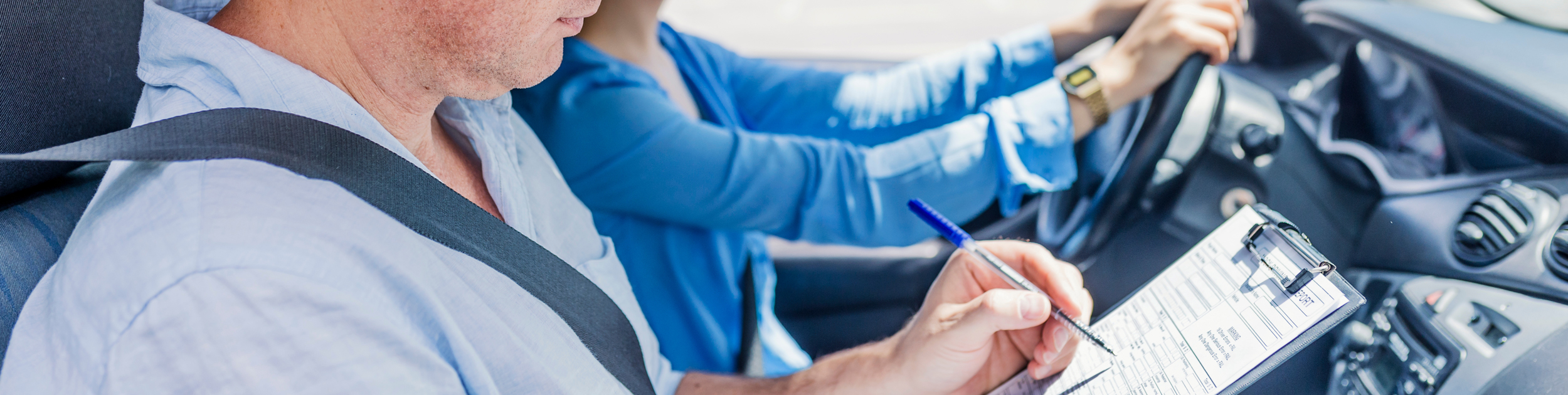 Driving Instructor making notes on clipboard while student drives with both hands on the wheel